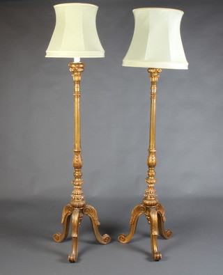 A pair of Italianate style carved and gilt painted standard lamps, raised on tripod supports 43cm h x 46cm complete with waisted green shades