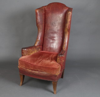 A Georgian style winged armchair upholstered in red leather and raised on outswept supports 