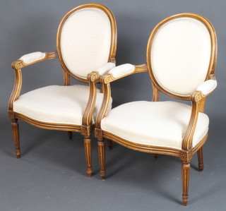A pair of beech framed French style open arm salon chairs with upholstered seats and backs raised on turned and fluted supports 