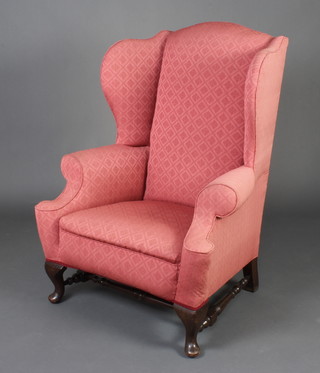 A Georgian style mahogany winged armchair upholstered in red material with turned stretcher, raised on cabriole supports 