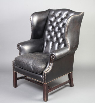 A Georgian style winged armchair upholstered in black buttoned leather, raised on square supports with H framed stretcher 