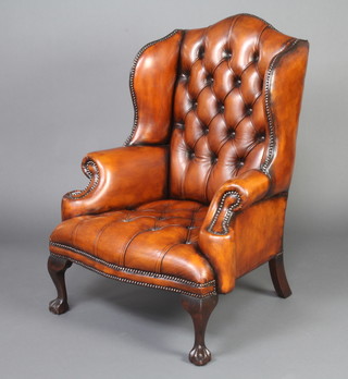 A Georgian style winged armchair upholstered in brown leather, raised on cabriole supports 