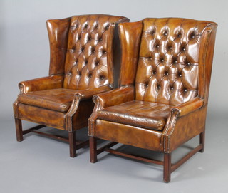 A pair of Georgian style winged armchairs upholstered in brown buttoned leather, raised on square supports with H framed stretcher 