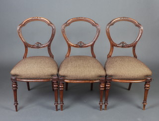 A set of 3 Victorian carved walnut balloon back dining chairs with carved and pierced mid rails and over stuffed seats, raised on turned and fluted supports 