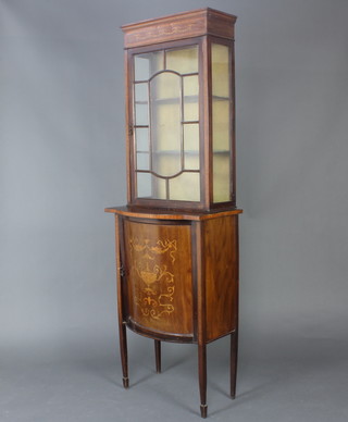 An Edwardian inlaid mahogany bow front display cabinet, the upper section enclosed by astragal glazed doors, the base enclosed by a panelled door, raised on square supports, spade feet 200cm h x 65cm w x 39cm d 