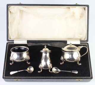 A silver 3 piece condiment raised on lion mask knees and paw feet with blue glass liners and 2 spoons, Birmingham 1969 cased, together with a silver butter spoon, 250 grams
