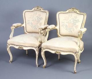 A pair of cream and gilt painted French open arm salon chairs, the seats and backs upholstered in gold material, raised on cabriole supports 