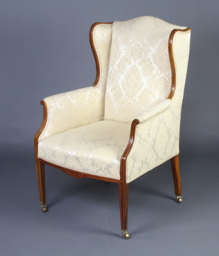 An Edwardian inlaid mahogany open arm chair upholstered in yellow material, raised on square supports ending in brass caps and casters 