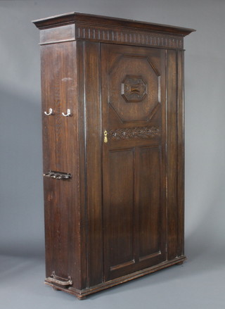 A 1920's oak hall cupboard with moulded cornice and arcaded decoration enclosed by a panelled door, raised on bun feet and having a J Rowland's patent umbrella stand to the side with 3 later hooks to the side 190cm h x 128cm w x 44cm d 