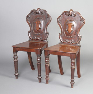 A pair of Victorian carved mahogany shield back hall chairs with solid seats, raised on turned supports 