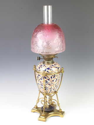 A Victorian ceramic oil lamp with floral reservoir and pink glass shade raised on a quatrefoil brass base, having a lear chimney 65cm 
