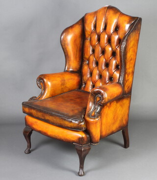 A Georgian style winged armchair upholstered in brown buttoned leather, raised on cabriole supports 