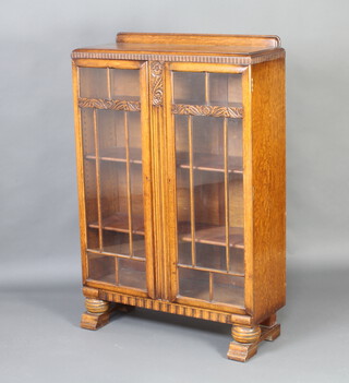 An Art Deco light oak display cabinet with raised back, interior fitted adjustable shelves enclosed by astragal glazed panelled doors, raised on cup and cover supports 127cm h x 84cm w x 30cm d 