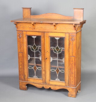 An Art Nouveau oak display cabinet with raised back fitted a shelf, the shelved interior enclosed by lead glazed panelled doors and with tulip repeat to the side 125cm h x 104cm w x 34cm d 