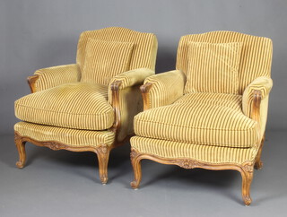 A pair of French walnut show frame armchairs upholstered in gold striped material raised on cabriole supports