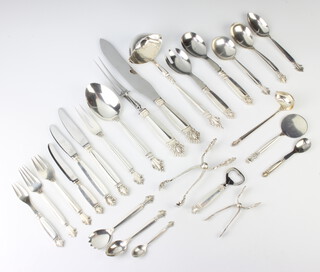 A Georg Jensen No.180 Acanthus/Konigin canteen of cutlery designed by Johan Rohde, produced between 1945 and 1976 comprising 7 egg spoons, 11 tea spoons, 12 dessert spoons, 12 soup spoons, 4 serving spoons, 2 table spoons, 4 sundae spoons, 2 ladles, 1 large ladle, 2 small sauce ladles, 3 round serving spoons, 12 small serving spoons, a pair of fish servers, a caddy spoon, sifter spoon and 2 other spoons, 12 fish knives, 12 fish forks, 11 small forks, 10 side forks, 12 dessert forks, 11 cake forks, 8 pickle forks, a cake slice, 7 mixed forks,  6 knife rests, a pair of ice nips, a pair of sugar nips and a scoop, 6466 grams, together with 9 silver handled small spoons, 2 pairs of silver handled salad servers, a pair of scissors, a bottle opener, a cheese slice, a bottle opener, 11 silver handled dinner knives, 12 silver handled side knives, 12 silver handled dessert knives, a pair of silver handled carvers,a cheese knife and 2 butter knives