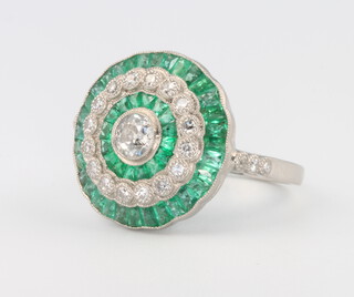 A platinum, emerald and diamond target dress ring set with a brilliant cut diamond surrounded by calibre cut emeralds, brilliant cut diamonds and calibre cut emeralds, diamonds approx. 1ct, emeralds 2.95ct, size P 