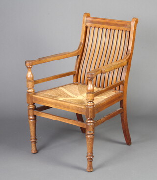 An Edwardian Arts and Crafts mahogany stick and rail back carver chair with woven rush seat, raised on turned supports, the back right hand leg impressed 182 