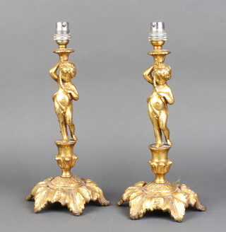 A pair of gilt metal table lamps in the form of standing cherubs raised on circular rococo bases 30cm h x 17cm 