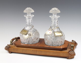 A pair of mallet shaped decanters and stoppers on a carved walnut stand with 4 spirit labels  