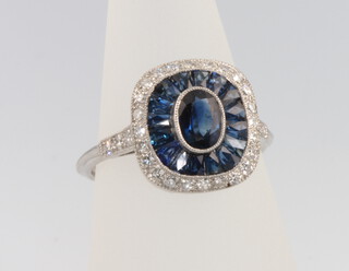 A platinum Art Deco style sapphire and diamond ring, the centre oval cut stone surrounded by calibre cut sapphires 1.7ct enclosed by brilliant cut diamonds 0.38ct, size L 1/2