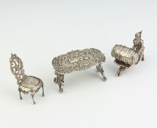 A Dutch cast silver miniature table decorated with a lady in a garden 6cm, a ditto of a dining chair 5.5 cm and a gnome pushing a barrel in a wheelbarrow 5.5cm 