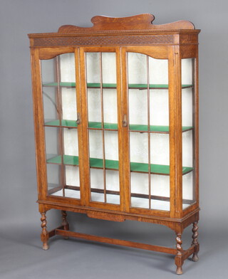 A 1930's oak bookcase, the raised back with blind fretwork frieze fitted shelves enclosed by astragal glazed panelled doors, raised on spiral turned block supports with H framed stretcher 174cm h x 119cm w x 34cm d 