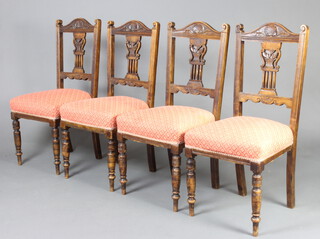 A set of four Edwardian carved walnut stick and rail back dining chairs with pierced slat backs and over stuffed seats, raised on turned supports 