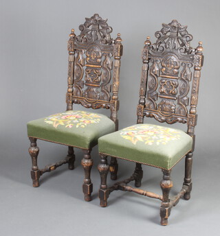 A pair of Victorian Carolean style carved and pierced oak high back hall chairs with Berlin woolwork seats raised on turned cup and cover supports with H framed stretcher 