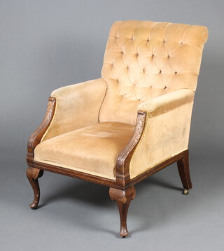 A Victorian mahogany carved show frame library chair upholstered in light coloured buttoned material, raised on cabriole supports 