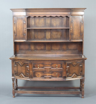 A 1920's Jacobean style oak dresser with moulded cornice, the upper section fitted 2 shelves flanked by cupboards above a recess, the base fitted 2 drawers and a pair of cupboards, raised on turned and block supports 182cm h x 153cm w x 50cm d  