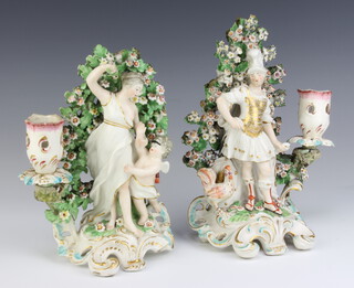 A pair of 19th Century Continental candlesticks with classical figures standing before bocage, raised on rococo bases 21cm 