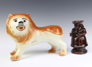 A 19th Century Staffordshire treacle glazed jug in the form of a standing Mrs Philpotts with bottle and glass 20cm h together with a ditto standing figure of a lion with glass eyes 25cm h x 25cm 
