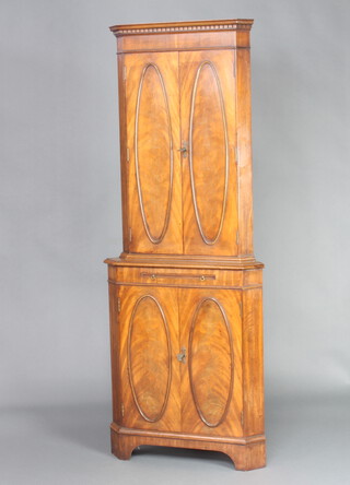 A Georgian style mahogany corner cocktail cabinet, the upper section with moulded and dentil cornice, fitted shelves enclosed by oval panelled doors, the base fitted a mirrored brushing slide above cupboards enclosed by panelled doors, raised on bracket feet 174cm h x 66cm w x 47cm d 