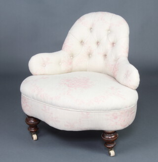 A Victorian shaped nursing chair upholstered in pink floral patterned material, raised on turned supports with ceramic casters 