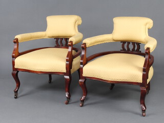 A pair of Edwardian show frame mahogany tub back arm chairs upholstered in yellow material, raised on cabriole supports  