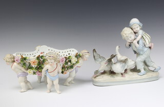 A Meissen style boat shaped ribbon ware floral encrusted basket supported by cherubs 15cm x 32cm x 24cm (some minor chips to roses) together with a 19th Century Continental porcelain figure group of 2 children encountering geese, raised on an oval base, impressed 11826 23cm x 28cm x 9cm 