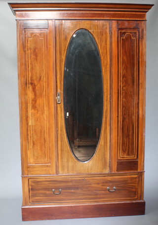 An Edwardian inlaid mahogany wardrobe with moulded cornice enclosed by an oval bevelled plate mirror panelled door, the base fitted a drawer and raised on a platform base 144cm h x 129cm w x 52cm d 