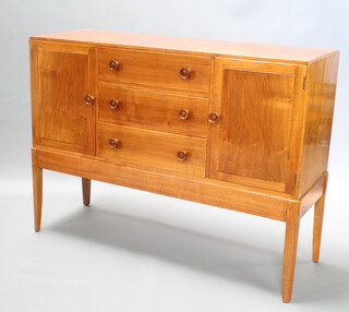 A 1950's Gordon Russell style walnut sideboard, fitted 3 drawers flanked by cupboards, raised on outswept supports 102cm h x 137cm w x 46cm d, purchased at Heals  
