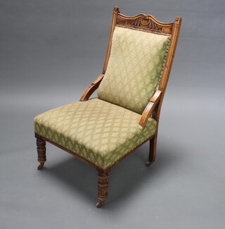 A Victorian carved walnut show frame nursing chair upholstered in green material raised on turned supports 