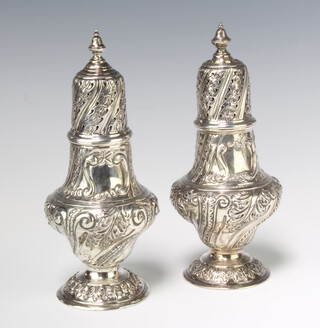 A matched pair of Edwardian repousse silver shakers with vacant cartouches, decorated with flowers and leaves, London 1902 and 1903, 19cm, 400 grams