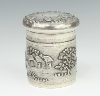 An engine repousse silver circular lidded box decorated with figures in a village setting 9cm, 232 grams