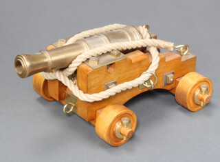 A 1 1/4" bore bronze model of a Naval ships canon with 17 1/2" long barrel, mounted on a solid beech Admiralty pattern (1800), the carriage with brass fittings and breeching ropes on solid beech trucks