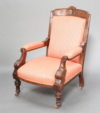 A Victorian carved walnut open armchair upholstered in striped pink material, raised on turned supports with ceramic casters 