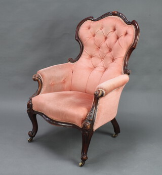 A Victorian carved mahogany show frame armchair upholstered in pink buttoned Dralon, raised on cabriole supports and brass casters (frame loose) 