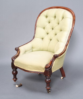 A Victorian mahogany show frame armchair upholstered in green buttoned material raised on turned supports ending in ceramic and brass casters (1 loose) 