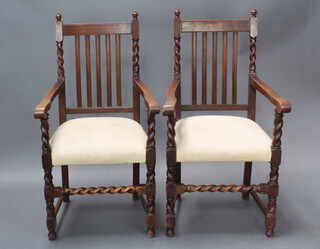 A pair of 1920's oak stick and rail back carver chairs with upholstered over stuffed seats, raised on turned and block supports 