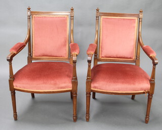 A pair of French Empire style walnut open arm chairs raised on turned supports, the seats and backs upholstered in rose coloured material 