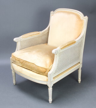 An Empire style white painted double cane bergere armchair, the seat and back upholstered in gold material, raised on turned and fluted supports 