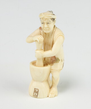 A Japanese ivory Meiji period Netsuke in the form of a standing man grinding flour in a double ended pot with coloured highlighted decoration, signed 5.5cm 